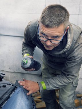 Neşeli, gözlüklü genç adam garaja bir araba boyuyor.