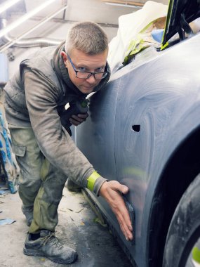 Neşeli, gözlüklü genç adam garaja bir araba boyuyor.