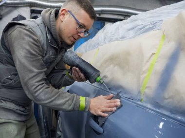 Neşeli, gözlüklü genç adam garaja bir araba boyuyor.