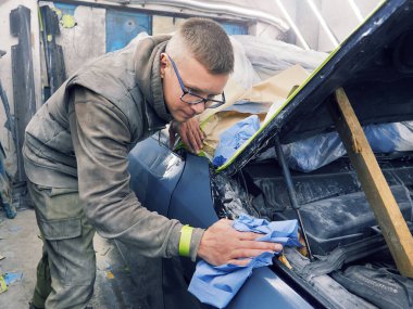 Neşeli, gözlüklü genç adam garaja bir araba boyuyor.