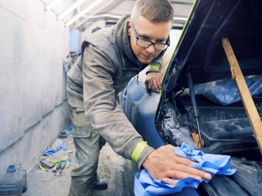 Neşeli, gözlüklü genç adam garaja bir araba boyuyor.