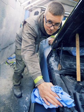 Neşeli, gözlüklü genç adam garaja bir araba boyuyor.