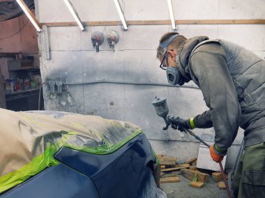 Neşeli, gözlüklü genç adam garaja bir araba boyuyor.