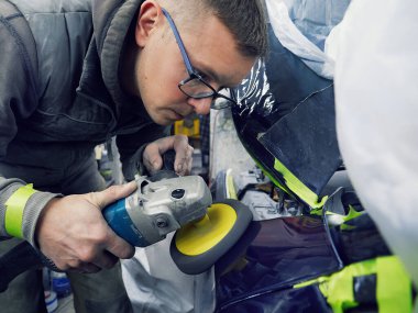 Neşeli, gözlüklü genç adam garaja bir araba boyuyor.