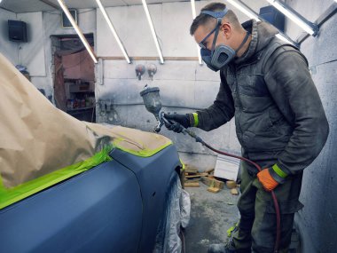 Neşeli, gözlüklü genç adam garaja bir araba boyuyor.