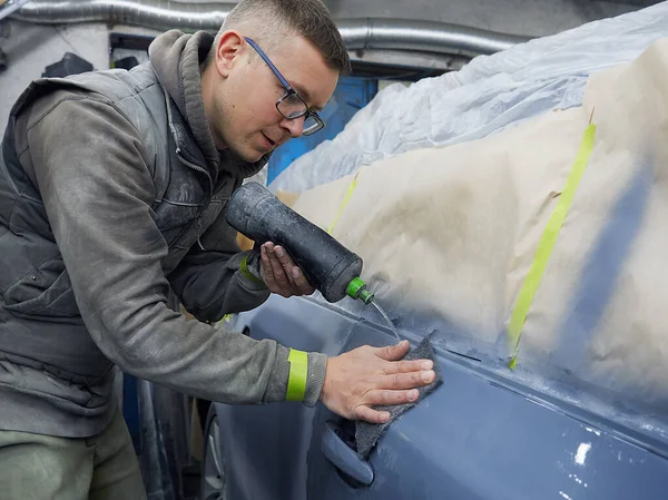 Neşeli, gözlüklü genç adam garaja bir araba boyuyor.