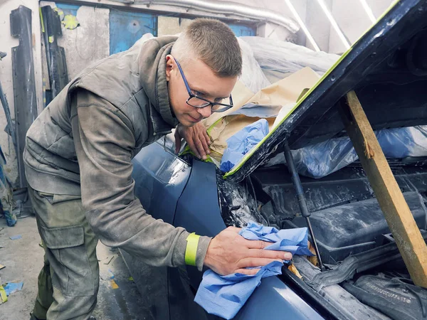 Neşeli, gözlüklü genç adam garaja bir araba boyuyor.