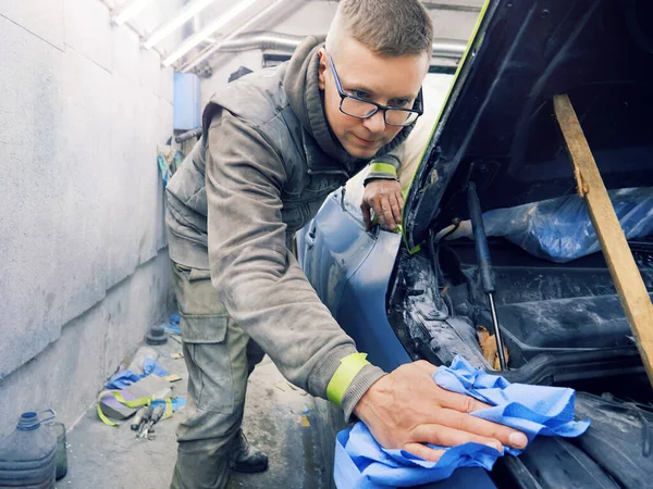 Neşeli, gözlüklü genç adam garaja bir araba boyuyor.