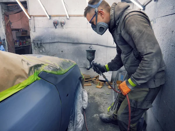 Neşeli, gözlüklü genç adam garaja bir araba boyuyor.