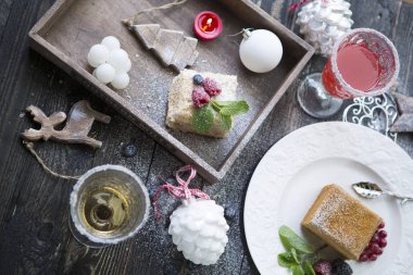 Noel pastaları, şampanyalar ve Noel oyuncakları, böğürtlenler, nane ve şeker tozuyla süslenmiş kuyruk kuyrukları. Ahşap arka planda yakın plan.