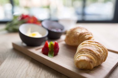 Masadaki sepetin içinde kruvasanla kahvaltı. Arka plandaki pencere. Çiçekler, sabah