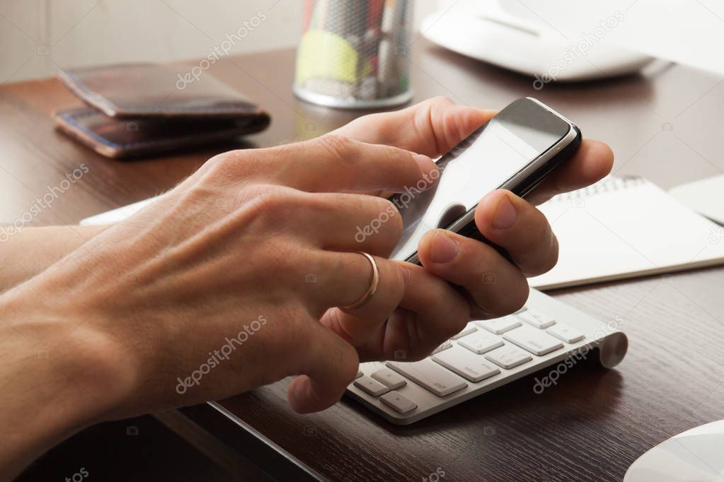 Male hands with phone in office. 