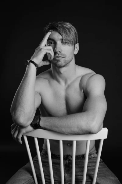 Muskularny i sprawny młody kulturysta fitness męski model pozowanie na krześle. Czarno-białe zdjęcie. — Zdjęcie stockowe