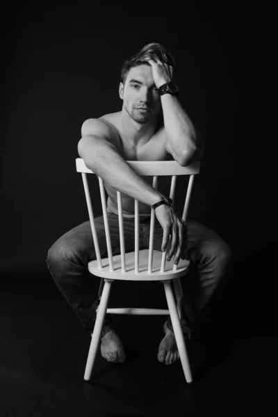 Muskularny i sprawny młody kulturysta fitness męski model pozowanie na krześle. Czarno-białe zdjęcie. — Zdjęcie stockowe
