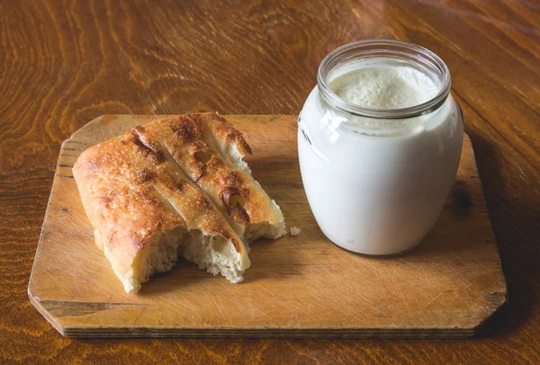 Sour milk in a glass jar with a piece of asian pita bread on a wooden board