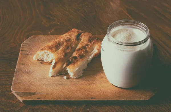 Sour milk in a glass jar with a piece of asian pita bread on a wooden board