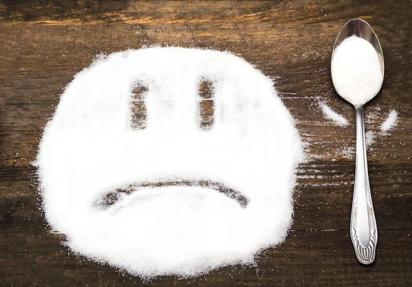 Gesicht eines traurigen Smileys aus Kristallzucker. Das Bild veranschaulicht den Schaden des Verzehrs von Zucker und Salz sowie die Abhängigkeit von Aromazusätzen. — Stockfoto