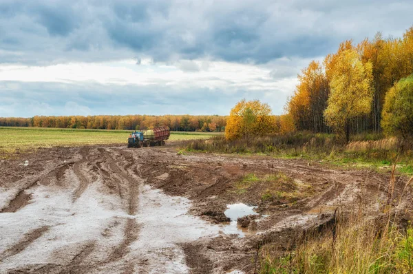 Traktor mit Anhänger nach Regenwetter im Gelände, herbstliche ländliche Landschaft lizenzfreie Stockfotos