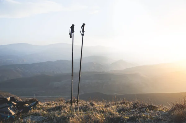 Subir às montanhas, bengalas nórdicas e uma mochila, um conjunto de viajantes. Maravilhoso pôr do sol no fundo Fotografia De Stock