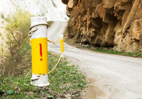 Fencing posts on a steep section of a narrow mountain road with a warning