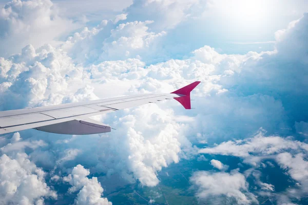 cloudy sky and red airplane wing as seen through window on aircr