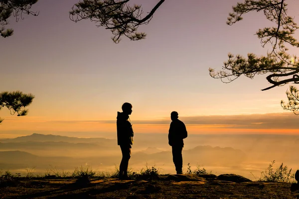 Homem de reboque de silluato levantar a mão e de pé durante o pôr do sol no topo — Fotografia de Stock