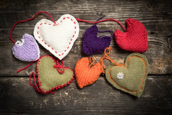 Colorful knitted hearts on the dark old boards