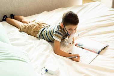 Evde kalıp koronavirüs salgınını önleyin. Çocuk tedavi sırasında ev ödevini bir nibulizörle yapıyor. Önleme salgını. COVID-19.