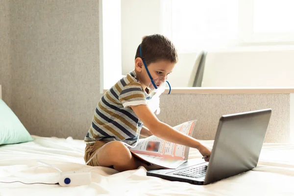 Stay at home quarantine coronavirus pandemic prevention. A child learns home lessons in an oxygen mask with a nibulizer, laptop and a book during quarantine. Prevention epidemic. COVID-19.