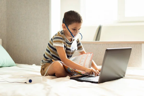 Stay at home quarantine coronavirus pandemic prevention. A child learns home lessons in an oxygen mask with a nibulizer, laptop and a book during quarantine. Prevention epidemic. COVID-19.