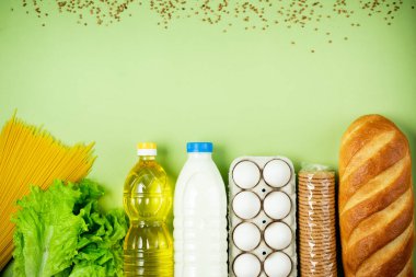 Temel taze ürünler yeşil arka planda yatar. Yumurta, yeşillik, spagetti, ekmek, süt, tuvalet kağıdı, kurabiye, ayçiçeği yağı. Yemek teslimatı covid-19 salgını, bağış. Üst Manzara. Boşluğu kopyala.