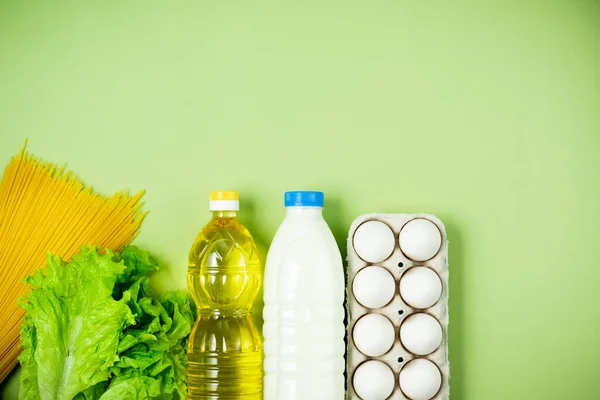 Essential fresh products lie on a green background. Eggs, greens, spaghetti, milk, sunflower oil. Food delivery covid-19 epidemic, Donation. top view. Copy space.