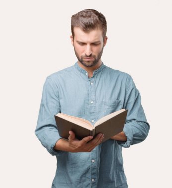 Genç yakışıklı adam, mavi kot gömlek, elinde bir kitap, sürpriz ya da mutlu ifade. Tek renkli arka planı izole kişi.