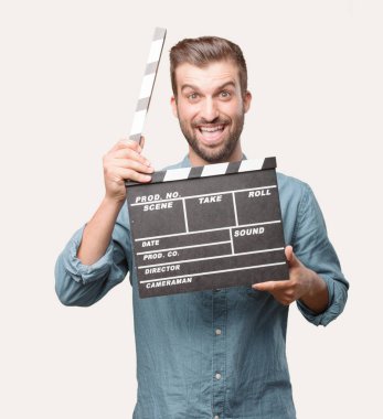 Bir mavi kot gömlek giymiş bir sinema clapper tutan yakışıklı delikanlı. Tek renkli arka planı izole kişi.