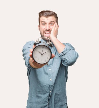 Yakışıklı delikanlı bir mavi kot gömlek giymiş bir çalar saat tutan vurguladı. Tek renkli arka planı izole kişi.