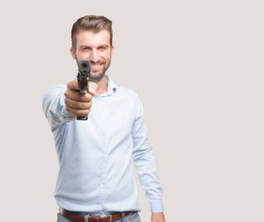 Yakışıklı delikanlı bir mavi t gömlek giymiş bir tabancayla. Tek renkli arka planı izole kişi.