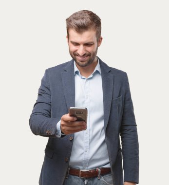 Genç yakışıklı işadamı bir smartphone, mavi ceket, memnuniyetini ifade ile mesaj yazarken. Tek renkli arka planı izole kişi.