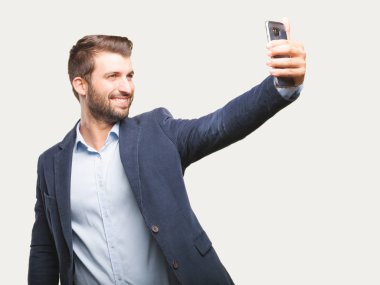 Bir selfie onun smartphone, mavi ceket ile alarak genç yakışıklı bir iş adamı. Tek renkli arka planı izole kişi.