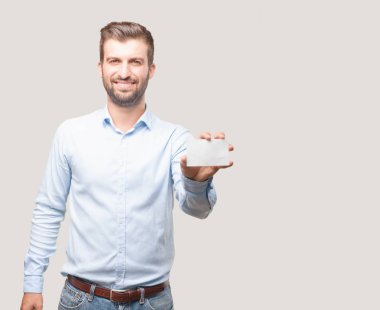 Genç yakışıklı adam, mavi t gömlek tutan bir ziyareti veya isim kartı, küçük boş placar. Satisified veya mutlu ifade. Tek renkli arka planı izole kişi.