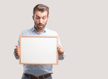 Kavramı, mavi t gömlek, yerleştirmek için boş bir afişini tutan genç yakışıklı adam ifade şaşırttı. Tek renkli arka planı izole kişi.