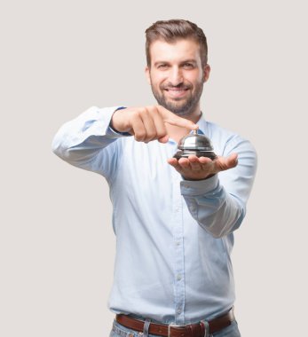 Genç yakışıklı adam, mavi tişörtlü mutlu ve gülümseyen bir halka bell holding. İfade destekler. Tek renkli arka planı izole kişi.