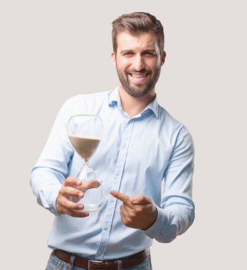 Genç yakışıklı adam mavi t gömlek giymiş bir kum saat timer ile korkuttu. Tek renkli arka planı izole kişi.