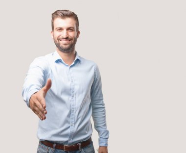 Yakışıklı delikanlı sallamak el jest mavi t gömlek giymiş selamlıyorum. Tek renkli arka planı izole kişi.