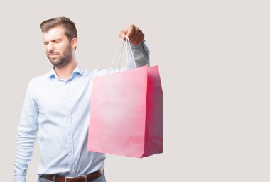 Genç yakışıklı adam, mavi tişörtlü, Holding alışveriş çantası sıkıcı. Tek renkli arka planı izole kişi.