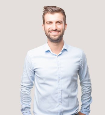 Yakışıklı genç gülümseyen, mavi tişörtlü, gurur ve memnun ifade. Tek renkli arka planı izole kişi.