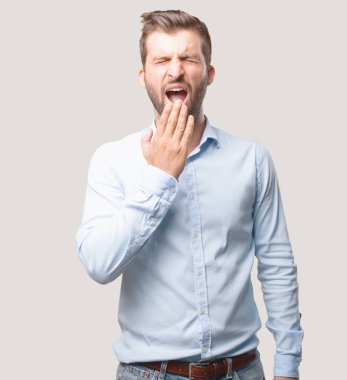 Genç yakışıklı esneme giyiyor mavi tişörtlü adam. Tek renkli arka planı izole kişi.