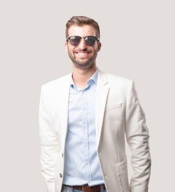 Genç yakışıklı işadamı ile güneş gözlüğü, beyaz ceket ve mutlu veya satiscfaction ifade. Tek renkli arka planı izole kişi.