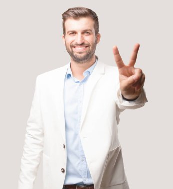 genç yakışıklı işadamı zafer işareti, beyaz ceket ve mutlu ifade. Tek renkli arka planı izole kişi.