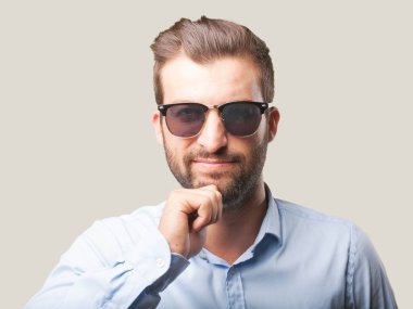 Bununla birlikte güneş gözlüklü bir mavi t-shirt giyen genç yakışıklı adam. Tek renkli arka planı izole kişi.