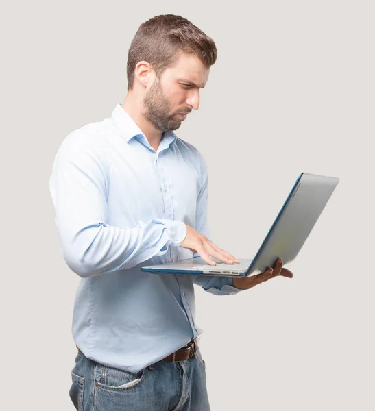 年轻英俊的男子带着一台手提电脑身穿蓝色 愤怒的表情 独立于单色背景的人 — 图库照片